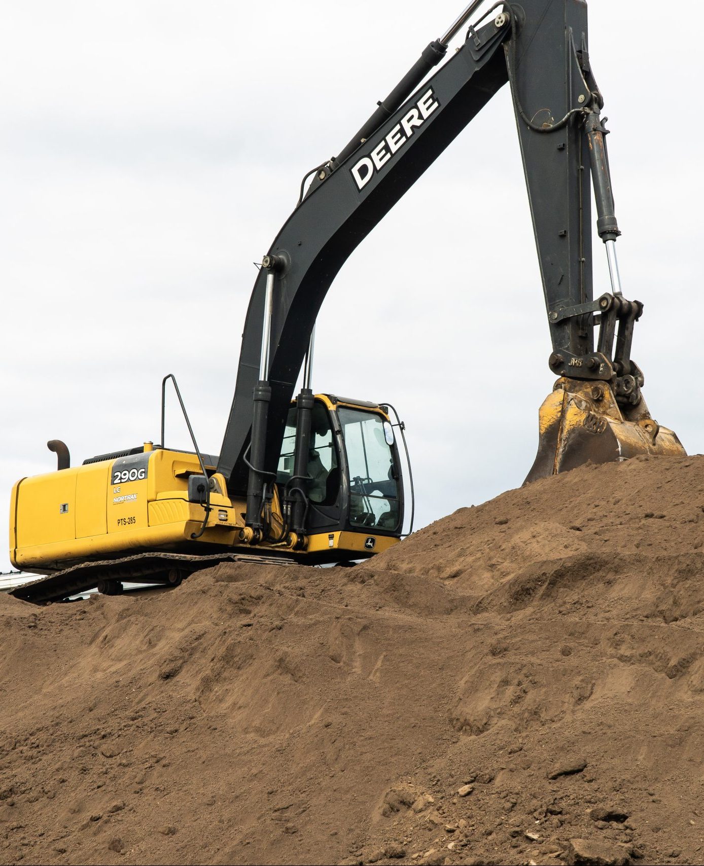 an excavator sits on top of a large pile of dirt that it's digging into