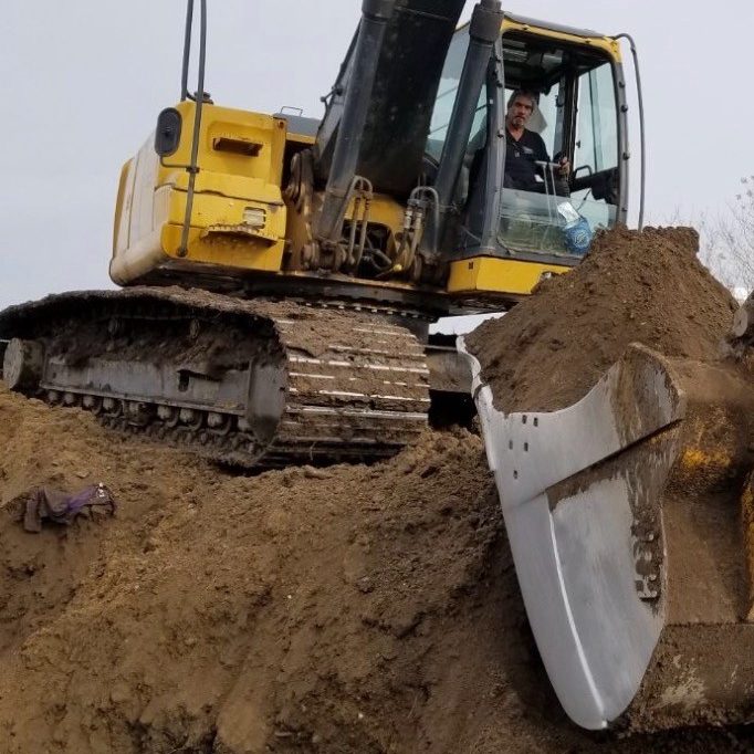 An excavator digs into a large pile of dirt